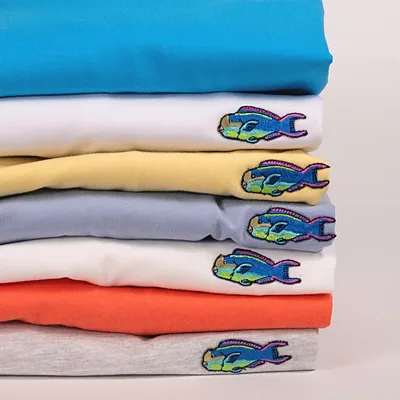 Pile de tee-shirts de couleur avec un écusson brodé poisson sur chacun